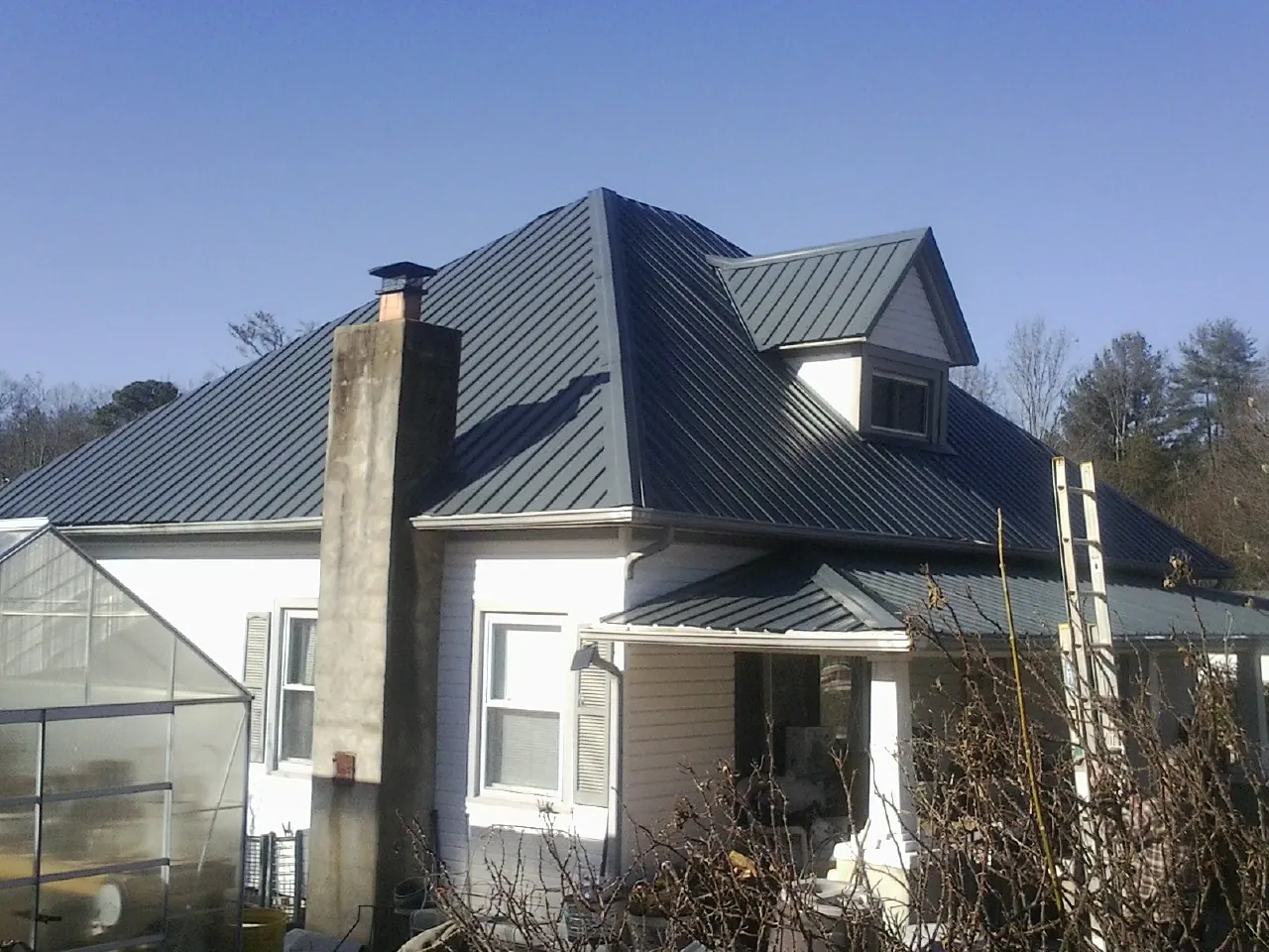 Dark blue standing seam metal roof on a white farmhouse with dormer — Slate & Tile Roof Repair by Roofing Brothers in Kilbourne