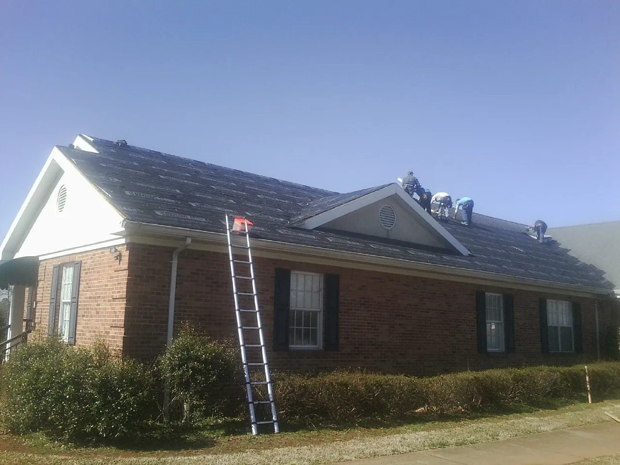 Crew tearing shingles off a brick ranch roof with a ladder set — Emergency Roof Repair work by our crew in Kilbourne