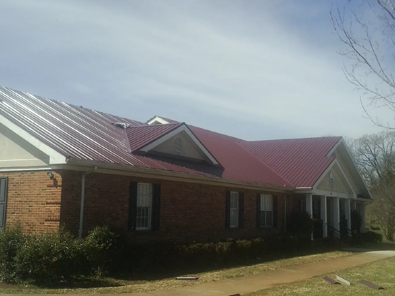 Red metal roof with gabled entries on a long brick building, from a Hail Damage Roof Repair job in Kilbourne