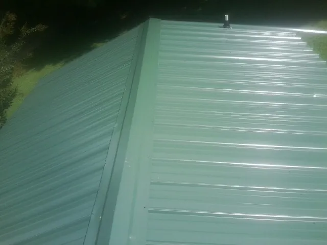 New green metal panels meeting at the ridge of a roof — Flat Roof Repair work by our crew in Kilbourne