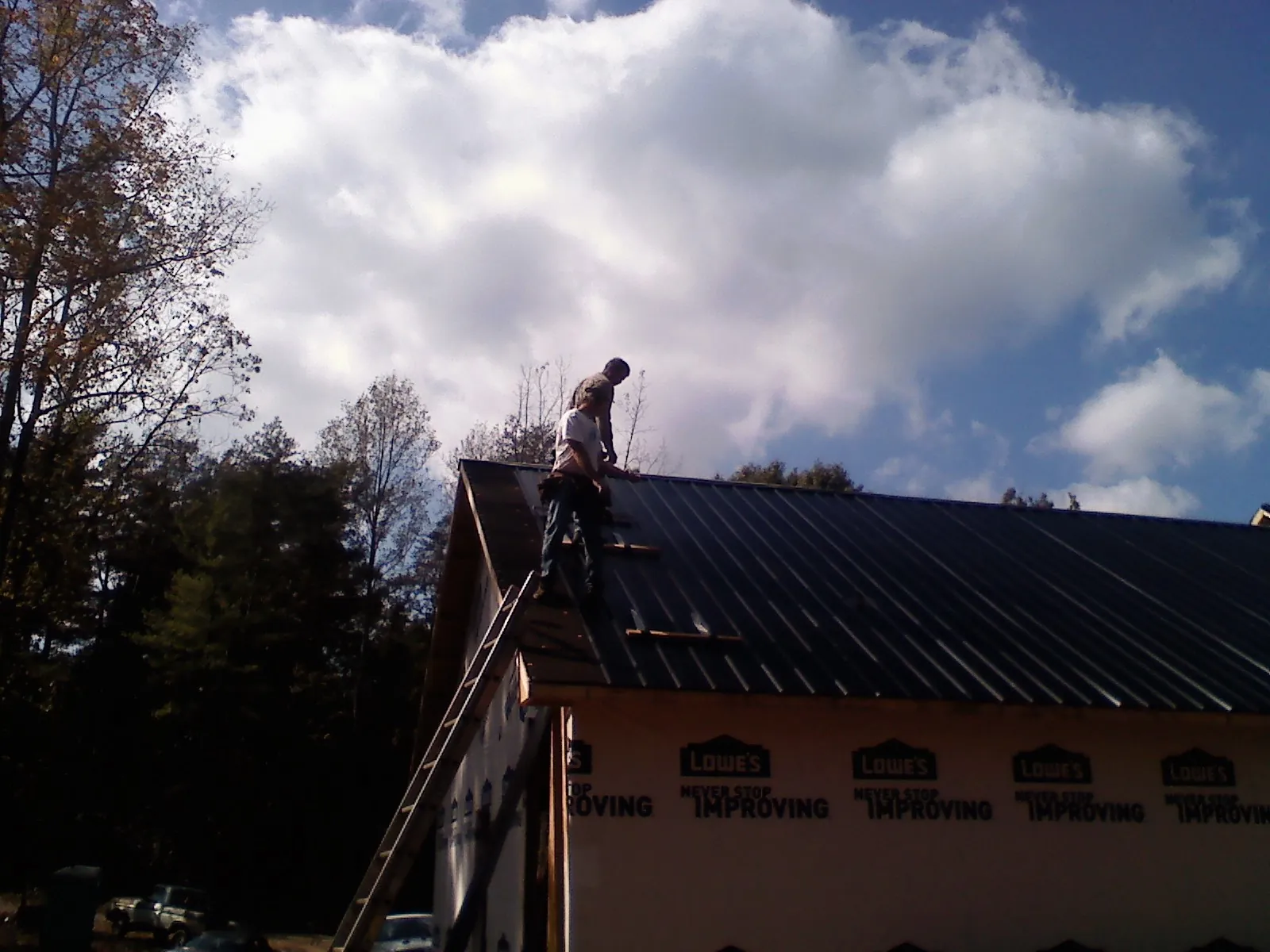 Roofer fastening dark metal panels high against a cloudy sky, from a Roof Inspection job in Kilbourne