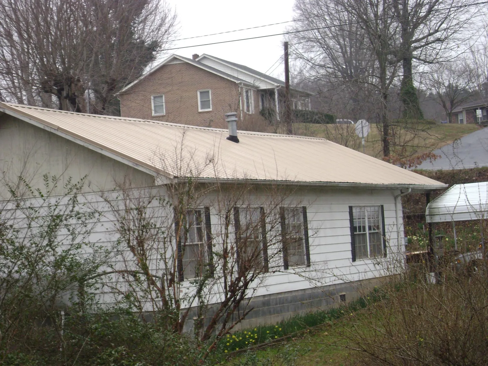 Tan metal roof on a white sided house set into a hillside — Commercial Roofing by Roofing Brothers in Kilbourne
